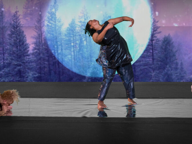 Kayla Hamilton stands on a reflective strip of silver, chin lifted as she arches her torso backwards, arms curved in front of her chest. Alice Sheppard sits on one end of the silver floor, torso folded into her own lap. Laurel Lawson lays on their back at the other end of the silver. Alice is a multiracial Black woman with short curly blonde hair; Kayla is a Black woman with shoulder length locs; Laurel is a white person with cropped hair. All three dancers wear dark shimmery bodysuits, a detailed video projection of a huge luminescent moon and a dense forest drenched in hues of cool blues and rich purples fills the background. Photo Cherylynn Tsushima