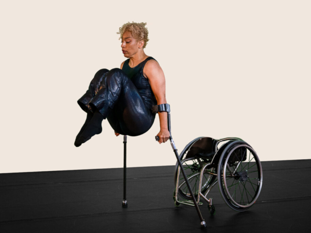 Alice Sheppard lifts and tucks her knees to her chest as she balances on her crutches. Her wheelchair rests on the floor behind her. Alice is a multiracial Black woman with coffee-colored skin and blonde curly hair piled atop her head; she wears a dark shimmery sleeveless bodysuit. The background is a soft cream tone.