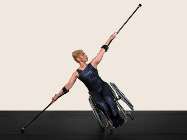 Alice Sheppard balances on one wheel as she tilts to one side and reaches her ultra-elongated crutches high above and to the side, creating a long diagonal line. She lifts her chin, gazing at her arm and crutch extended in the air. Alice is a multiracial Black woman with coffee-colored skin and blonde curly hair piled atop her head; she wears a dark shimmery sleeveless bodysuit. The background is a soft cream tone.